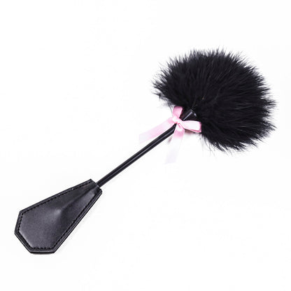Black faux leather spanking paddle with fluffy feather tickler and pink satin bow.